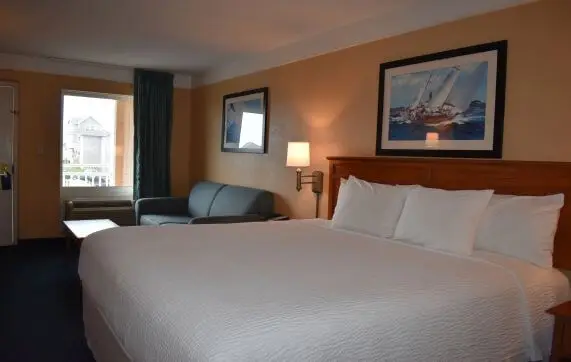 A king bed with white linens below two framed sailboat prints and a teal armchair, in a room furnished the same way as the property's standard king room