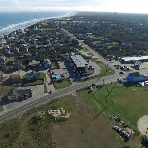 An aerial view of Highway 12 through Buxton, with the inn's pool and roofline visible among the village houses and the ocean beyond