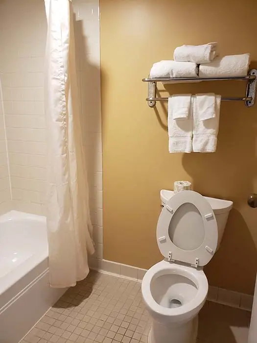A guest bathroom with a tub and shower, folded white towels on a wall rack, and the toilet beside it