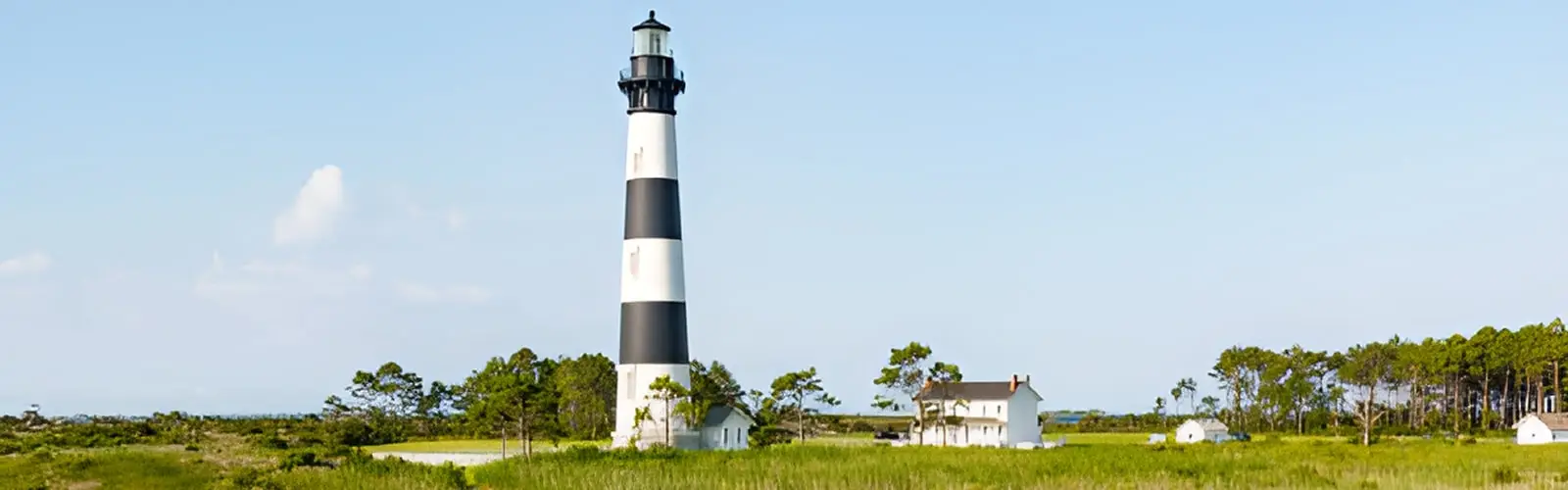 The black-and-white spiral-striped Cape Hatteras Lighthouse against a partly cloudy sky, seen across open grassland