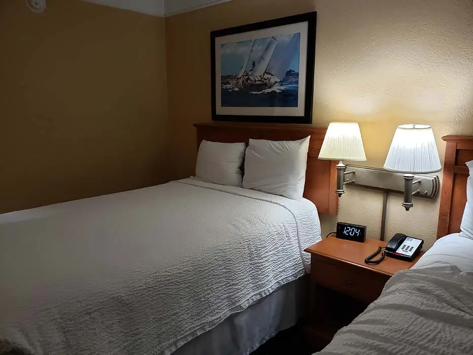 A king bed with a framed sailboat print above the headboard, beside a nightstand with a telephone and a digital clock
