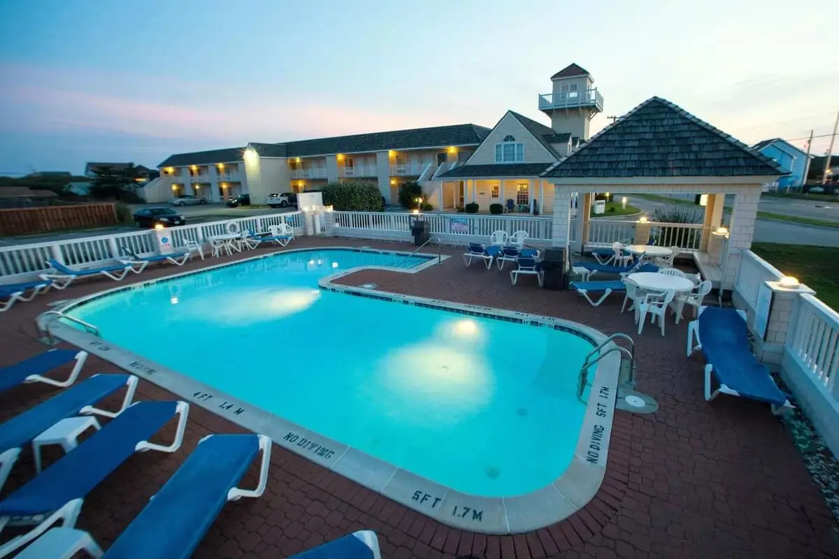 The Hatteras Island Inn’s shingled tower and guest wing lit up at dusk, with the outdoor pool in the foreground