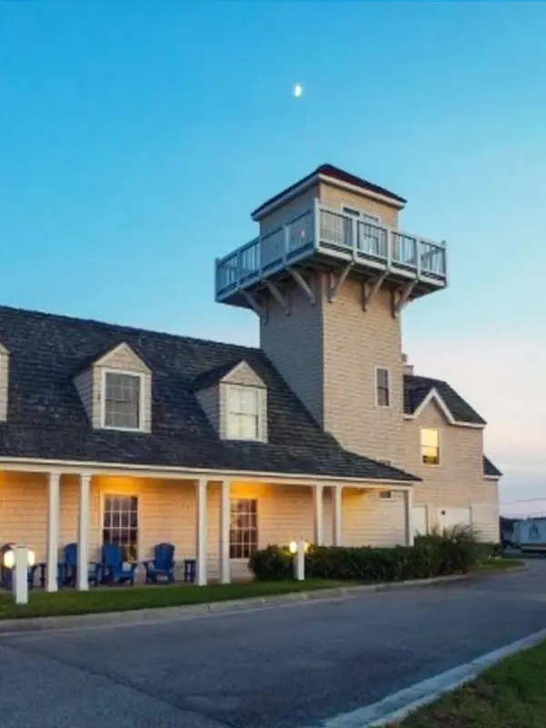 The Hatteras Island Inn's shingled tower and covered porch by daylight, with an 'Office' sign and blue Adirondack chairs